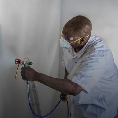 Muž používající stříkací zařízení na malování místnosti pomocí stříkacího zařízení.