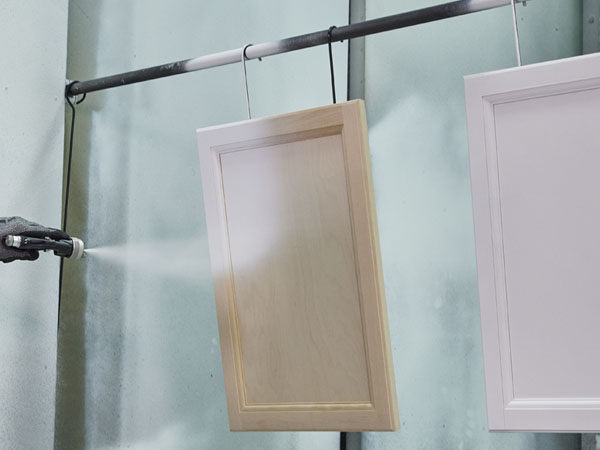 A paint booth operator coats wood cabinet doors with a air-assisted airless paint spray gun