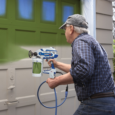 Homeowner painting a garage door with a paint sprayer