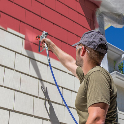 Photo d'une personne en train de peindre l'extérieur d'une maison avec un pulvérisateur