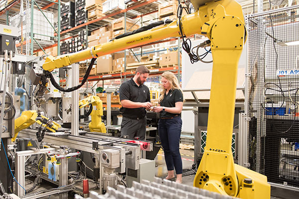 женщина и мужчина на заводе с роботом